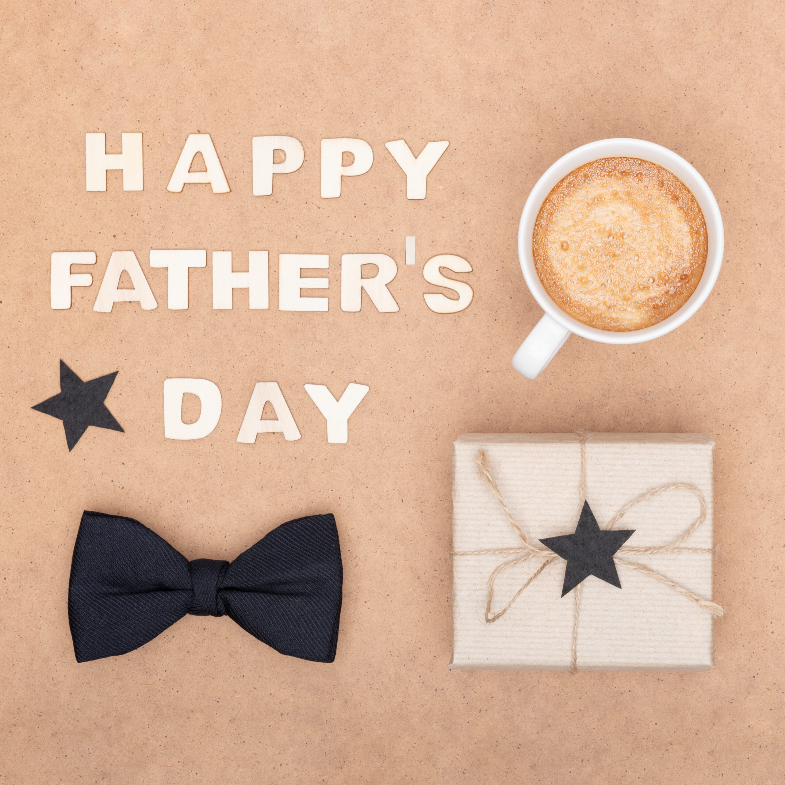 Happy Father's Day Background. Cup of coffee, beautiful present and black bow tie on brown background flat lay. Fathers day still life setup.